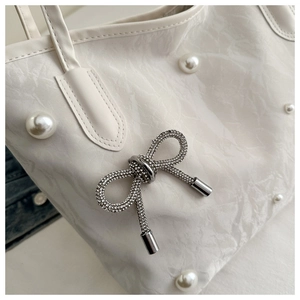 Detail of white tote bag featuring pleated texture with pearl accents and crystal bow