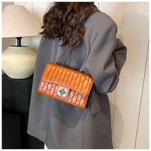 Detail of orange quilted crossbody bag featuring metal clover lock and chain strap