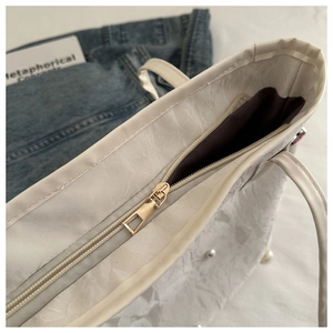Detail of creamy tote bag featuring pleated texture, pearl accents and gold metal zipper
