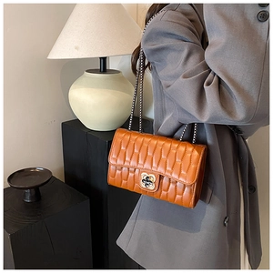 Detailed view of caramel orange quilted square bag with gold floral lock and chain strap