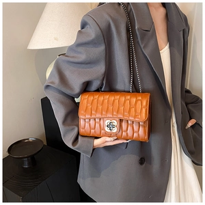Detail of caramel brown quilted chain bag with a floral metal clasp on a female model