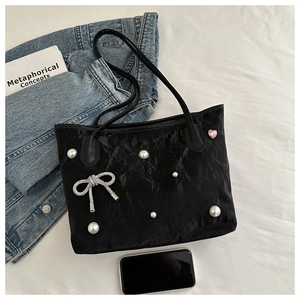 Detail of black pleated tote bag with pearl accents and a sparkling butterfly bow charm