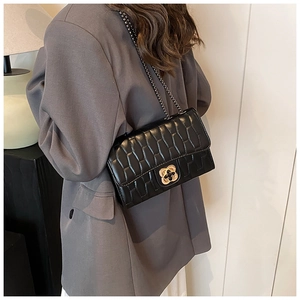 Detail of black quilted leather crossbody bag with golden petal metal buckle and chain strap