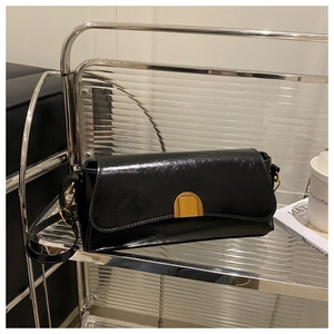 Detail of black glossy leather shoulder bag featuring a gold semi-cylindrical metal buckle