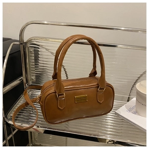 Detailed view of brown faux leather Boston bag with gold metal plaque on display stand
