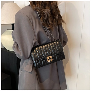Detail of black quilted shoulder bag with gold flower twist lock on a casual blazer