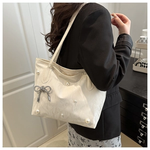 Détail du sac cabas plissé crème avec perles et pendentif nœud papillon argenté