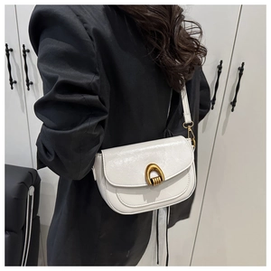White glossy leather shoulder bag featuring a gold U-shaped lock buckle worn with a black blazer