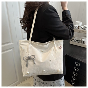 Détail du sac cabas blanc orné de perles et d'un nœud papillon argenté élégant