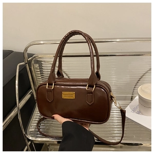 Detailed close-up of dark brown glossy leather handbag with gold plaque and crossbody strap