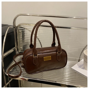 Detail of a dark brown glossy leather handbag featuring a vintage golden metal nameplate