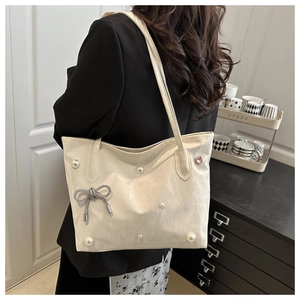 Side view of cream tote bag with pearl accents and silver bow charm on female model