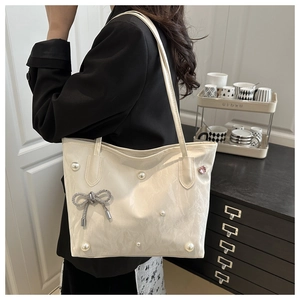Detail of white tote bag featuring decorative pearls and a silver bow with metal tassels