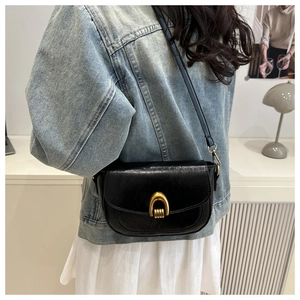Detail of a vintage black saddle bag showing its golden buckle and oil wax leather texture