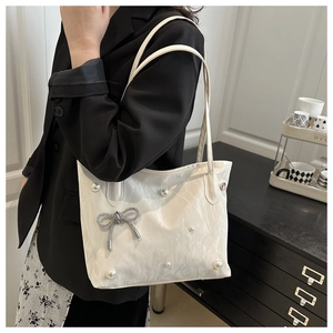 Detail of white marble-textured tote bag featuring pearl accents and a silver bow clasp