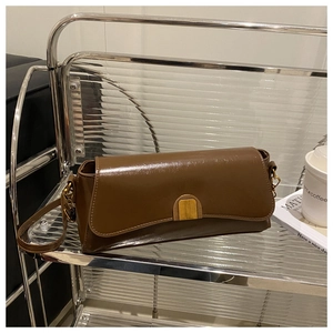 Detail of dark brown leather crossbody bag with golden clasp on an aesthetic glass shelf