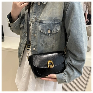 Close-up of black glossy leather crossbody bag with vintage gold U-shaped metal buckle