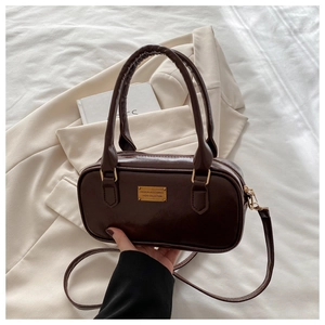 Detail of dark brown leather bowling bag with gold logo plaque on a beige blazer