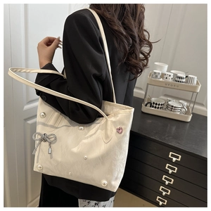 Detail of ivory tote bag with delicate texture, pearl accents, and a bow pendant