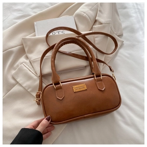 Detail of caramel brown faux leather handbag with gold metal plaque and top handle