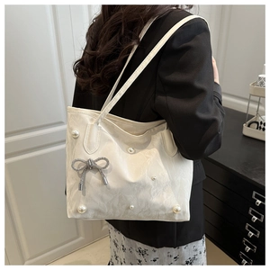 Détail du sac cabas crème avec des perles et un pendentif nœud papillon étincelant