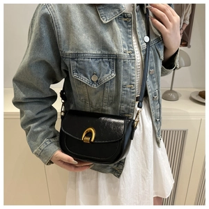 Detail of glossy black leather saddle bag with U-shaped gold hardware buckle shown on model