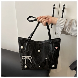 Detail of black pleated tote bag featuring pearl accents and rhinestone bow ornament