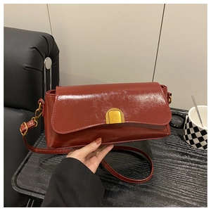 Close-up of deep red glossy shoulder bag with a gold semi-circle metal clasp detail
