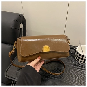 Close-up of brown glossy leather crossbody bag featuring an elegant gold arch metal clasp