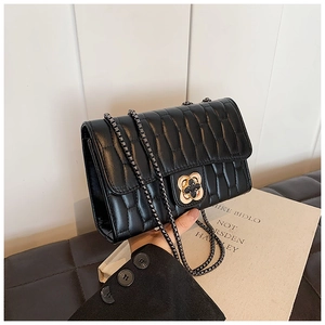 Détail d'un sac matelassé noir avec fermoir floral doré et bandoulière en chaîne
