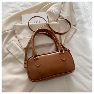 Brown leather crossbody bowling bag with gold hardware placed on a beige blazer
