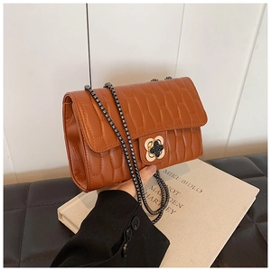 Detail of brown quilted crossbody bag featuring a floral clasp and gunmetal chain strap