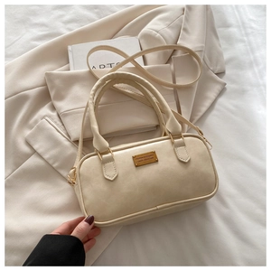 Detail of beige faux leather bowling bag with gold buckle on a neutral blazer background