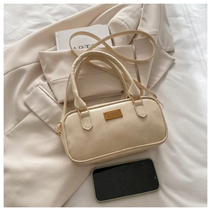 Close-up of cream leather bowling bag with gold plaque on a beige blazer background