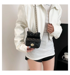 Detail of a black quilted mini crossbody bag with a large leather bow and gold chain strap