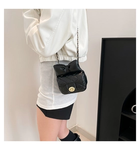 Close-up of black quilted leather crossbody bag with bow detail and gold chain strap