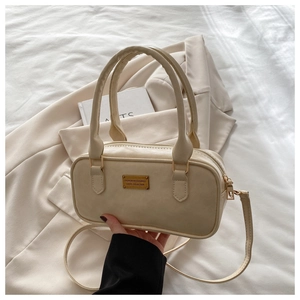 Detail of cream white faux leather bowling bag with gold hardware on beige blazer