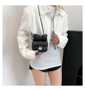 Model wearing a black quilted leather mini crossbody bag with a bow and chain strap