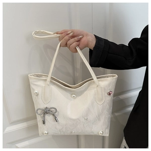 Detail of cream tote bag with pearl accents, rhinestone bow, and heart gem decoration