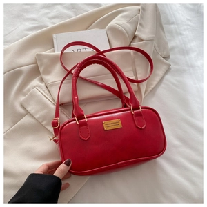 Detailed view of red leather bowling bag with gold logo plaque and adjustable shoulder strap