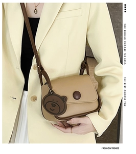 Detail of minimalist beige square crossbody bag with bear charm on model outfit