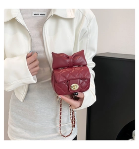Detail of burgundy quilted mini bag with oversized bow and golden metal twist lock closure