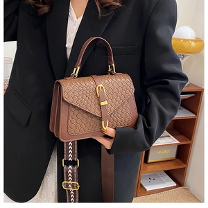 Detail of brown woven texture handbag with gold clasp and decorative wide strap