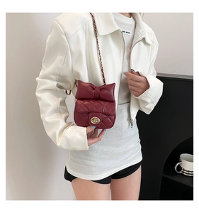 Close-up of wine red quilted handbag with oversized bow detail and metal twist lock