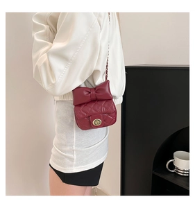 Detail of burgundy quilted crossbody bag with large leather bow and gold chain strap