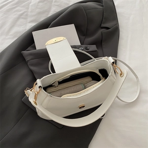 Minimalist white half-moon shoulder bag with wide strap and gold hardware on blazer