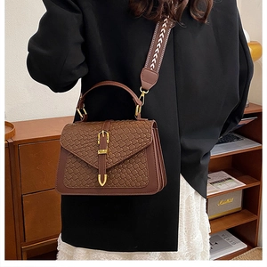 Detail of brown woven leather texture with gold buckle and embroidered wide shoulder strap