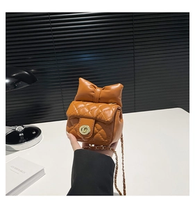 Detail of caramel quilted mini bag with bow decoration and gold metal chain strap