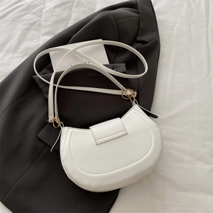 Minimalist white half-moon crossbody bag with gold hardware on a dark grey blazer