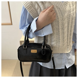 Close-up of black glossy leather bag featuring golden metal plate and adjustable strap